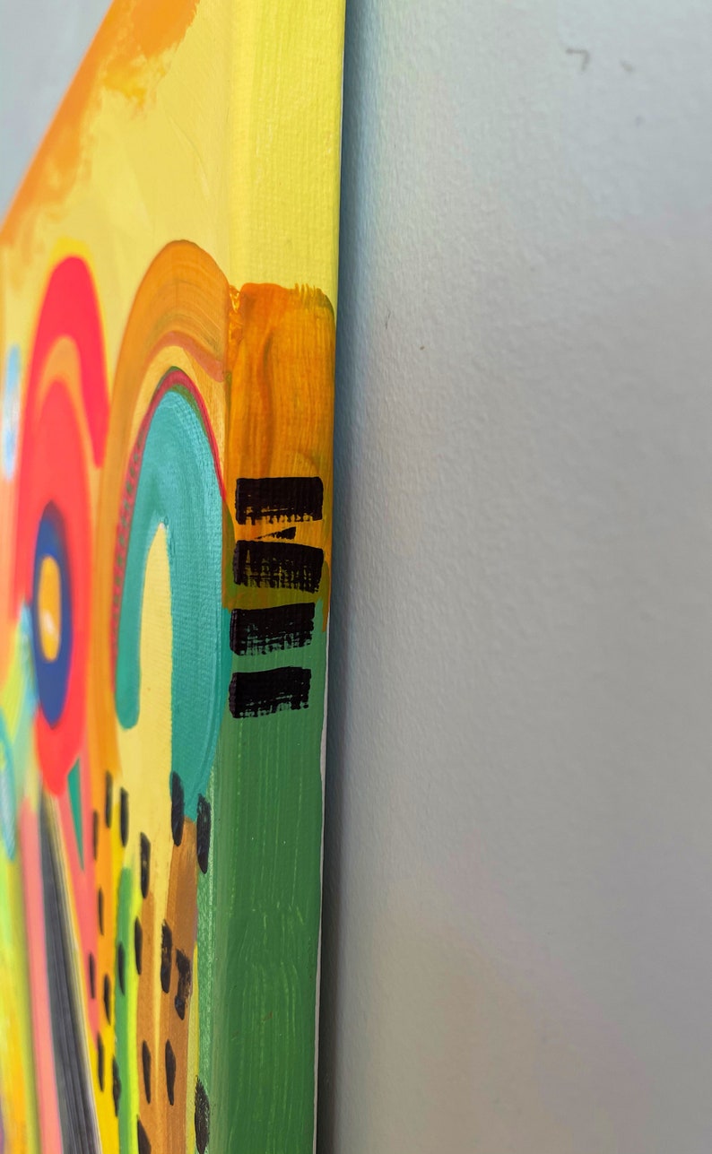 May include: Close-up of the side of a canvas painting with a colorful abstract design. The edges of the canvas are painted yellow, orange, green, and black.