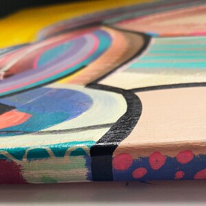 May include: Close-up of the edge of a colourful abstract painting on canvas. The painting features a variety of shapes and colours, including yellow, blue, pink, and green. The edges of the canvas are painted with a blue and pink polka dot pattern.