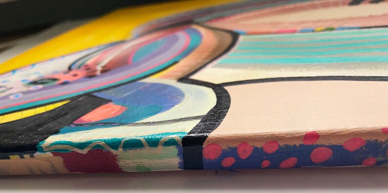 May include: Close-up of the edge of a colourful abstract painting on canvas. The painting features a variety of shapes and colours, including yellow, blue, pink, and green. The edges of the canvas are painted with a blue and pink polka dot pattern.