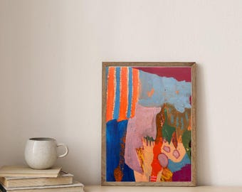 May include: A framed abstract painting featuring vertical orange and blue stripes, a large mauve shape, and patches of dark blue, green, and red. The artwork is displayed in a thin wooden frame, positioned next to a stack of books and a ceramic mug.