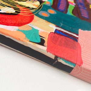 May include: A small, colorful abstract painting on canvas with a black frame. The painting features a variety of shapes and colors, including red, orange, yellow, green, blue, and purple. The painting is finished with a pink and white patterned paper border.