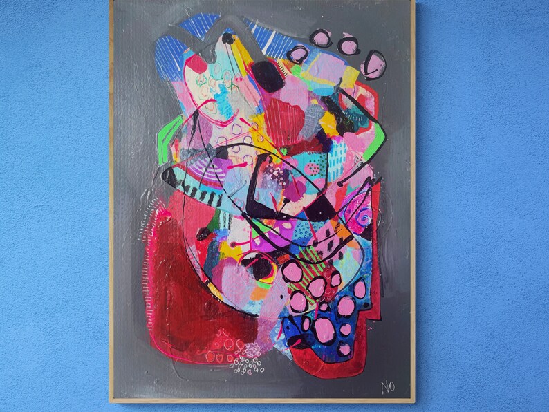 May include: Abstract painting with a colourful, layered design. The painting features a mix of pink, red, blue, green, black, and white colours. The painting is framed in a wooden frame.