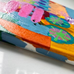 May include: A small, colorful abstract painting on canvas. The painting features a variety of shapes and colors, including pink, blue, green, orange, and yellow. The painting is framed with a blue border.