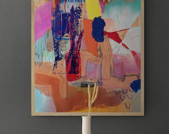 Puede incluir: Pintura abstracta en un marco de madera con un diseño colorido y en capas que presenta tonos de rosa, azul, amarillo, naranja y rojo. La pintura se exhibe en una pared gris con un jarrón blanco y flores secas delante.