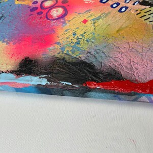May include: Abstract painting on canvas with a textured surface. The painting features a variety of colors, including pink, blue, yellow, red, and black. The edges of the canvas are painted in a light blue color.