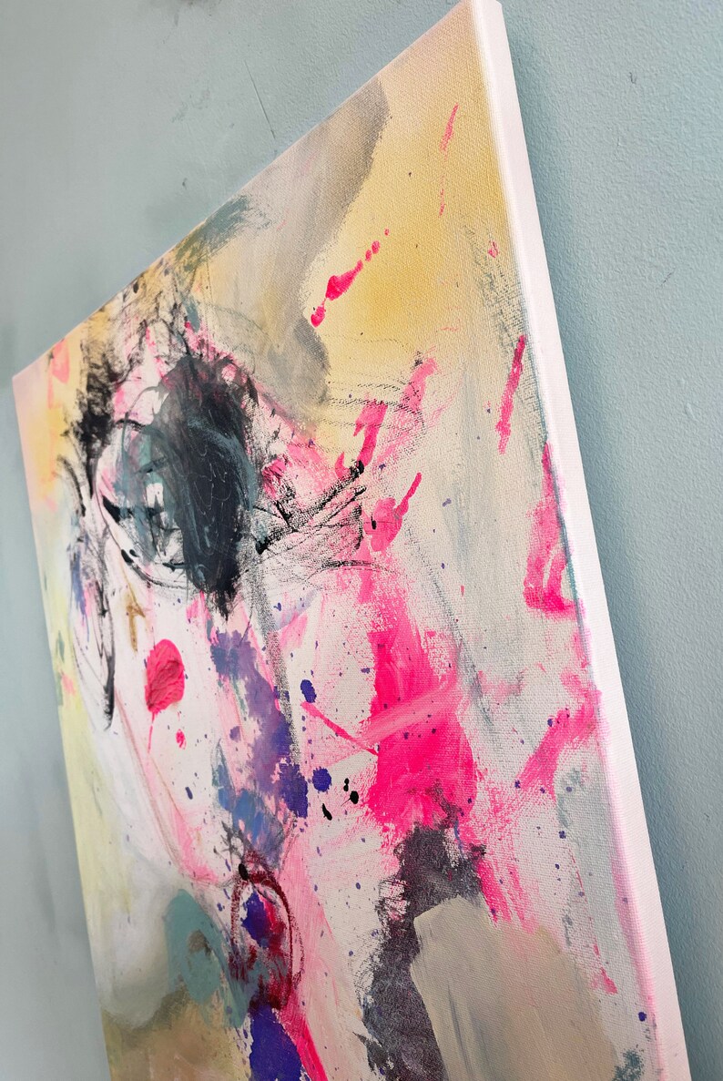 Puede incluir: Pintura abstracta sobre lienzo con salpicaduras de pintura rosa, amarilla, azul y negra. La pintura tiene una superficie texturizada y un fondo blanco.