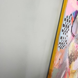 May include: A colorful abstract painting with a yellow frame. The painting features a variety of shapes and colors, including pink, blue, green, and black. The painting is textured and has a layered look.