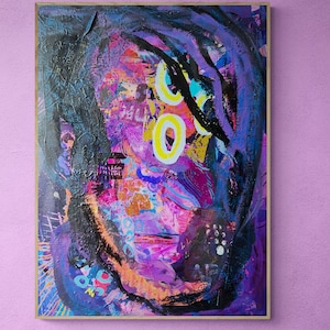 May include: Abstract painting of a person's face with purple, pink, blue, yellow, and black paint. The painting is framed in a wooden frame.