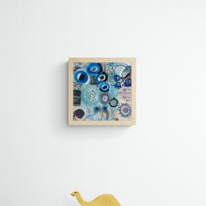 May include: A framed abstract painting in a blue, white and black colour scheme. The painting features a variety of shapes and patterns, including circles, swirls and lines. The frame is made of wood and has a natural finish.
