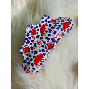 May include: A white plastic hair claw with a red, blue, and white football and buffalo design.