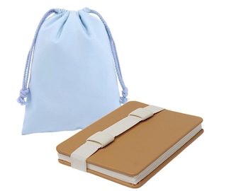 Puede incluir: Un cuaderno rectangular de color marrón claro con un cierre de banda elástica blanca, acompañado de una bolsa de tela azul claro con cordón y cuerdas trenzadas a juego para asegurar la abertura superior.