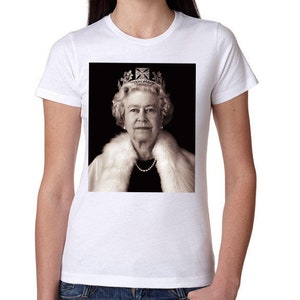 Può includere: Una t-shirt bianca a maniche corte con una stampa grafica rettangolare centrata della regina Elisabetta II. Il ritratto mostra la sovrana che indossa una corona, una collana di perle e una stola di pelliccia bianca su sfondo nero.
