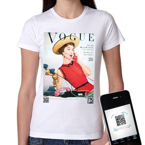 Può includere: Una t-shirt bianca a maniche corte con una stampa di una copertina di una rivista Vogue vintage. La grafica raffigura una persona con un vestito rosso e un cappello giallo che tiene un telefono rosso, circondata da vari telefoni. Due QR code in basso.