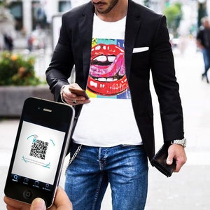 Può includere: Una t-shirt bianca con una grafica pop art colorata di labbra rosse e una lingua, indossata sotto un blazer nero con jeans blu. Uno smartphone nero in primo piano mostra un codice QR sullo schermo con il testo Scan the free Paperclip Phone app.