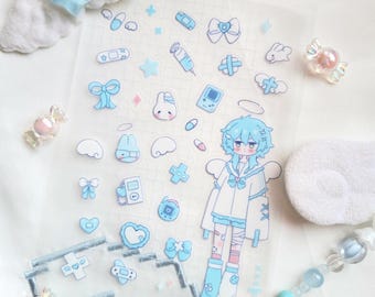 Puede incluir: Una hoja de pegatinas transparentes con varias ilustraciones azules y blancas, incluyendo lazos, corazones, cruces y un personaje de dibujos animados con pelo azul y alas de ángel. También se ven caramelos decorativos y un accesorio en forma de estrella.