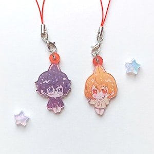 Peut inclure: Deux breloques de personnages d'anime colorés sur des lanières rouges. Les breloques sont en acrylique transparent avec un motif imprimé. Le personnage de gauche a les cheveux noirs courts et porte une tenue violette et noire. Le personnage de droite a les cheveux orange courts et porte une tenue blanche et marron.