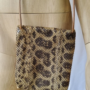 Puede incluir: Un pequeño bolso bandolera de piel de serpiente marrón y negro con una correa de cuero marrón.