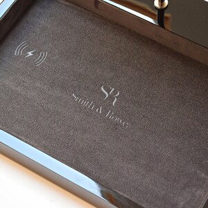 May include: A black tray with a gray felt lining. The tray has a wireless charging pad with a lightning bolt icon and the text "Smith & Jones" engraved on the felt.