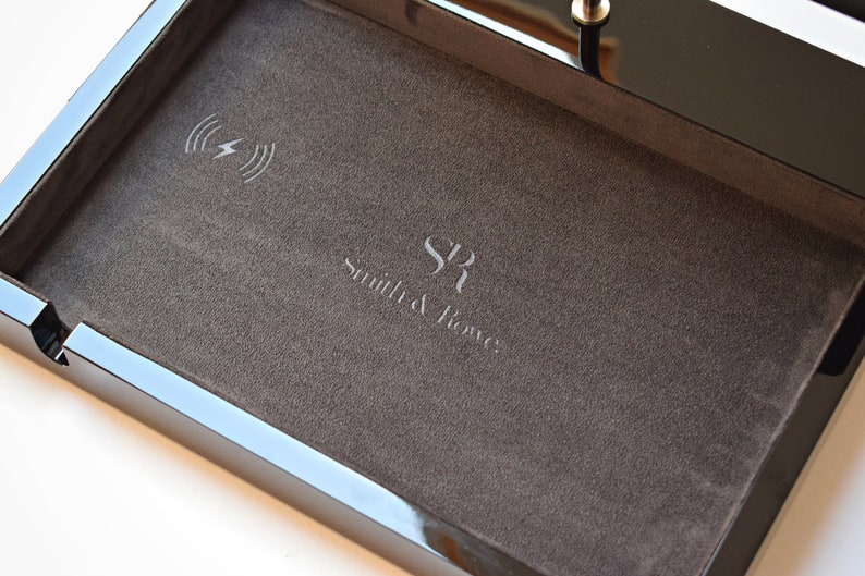 May include: A black tray with a gray felt lining. The tray has a wireless charging pad with a lightning bolt icon and the text "Smith & Jones" engraved on the felt.