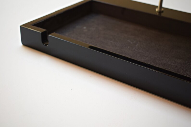 May include: A black rectangular tray with a black felt lining and a small slot on the side. The tray is made of wood and has a glossy finish.