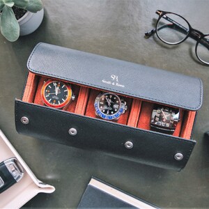 May include: A black leather watch roll with three watch slots and a red felt lining. The watch roll has the text "S1 Smith & Jones" embossed on the front.