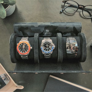 May include: A black watch roll with a camouflage pattern and the text "SR Smith & Jones" holds three silver wristwatches with black faces. The watches have different colored accents on the bezels.