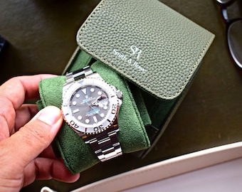 May include: A silver Rolex watch with a black face and a green watch case. The watch is in a green velvet watch case with the text "Smith & Rowe" on the case.