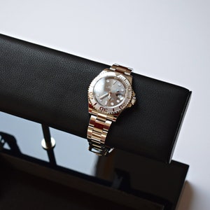 May include: Two silver wristwatches with black leather watch bands on a black display stand. The watch on the left has a blue bezel and the watch on the right has a silver bezel.