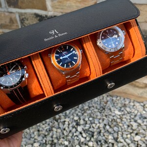 May include: Black leather watch roll with orange lining and three watches inside. The watch roll has the text "SR Smith & Rose" on the front.