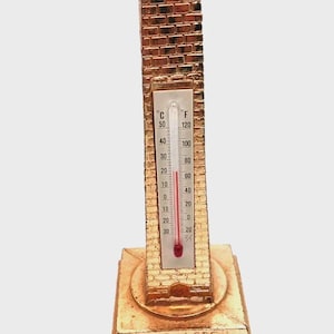 May include: A gold-colored thermometer shaped like a brick building, with a temperature reading of approximately 20 degrees Celsius and 68 degrees Fahrenheit. The base reads "WASHINGTON".