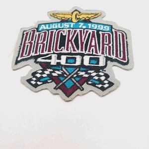 May include: Embroidered patch with the text "BRICKYARD 400" in maroon and black, with the date "AUGUST 7, 1999" above. Features a gold emblem and checkered flags in blue, maroon, and black.