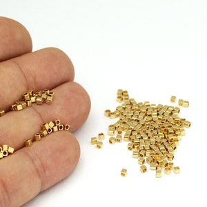 Op de afbeelding: Een grote stapel vierkante gouden kralen, waarvan sommige in een hand worden gehouden.