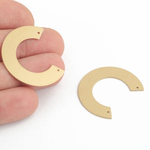 Op de afbeelding: Twee halfronde vormen van goudkleurig metaal met elk twee gaten. De vormen zijn plat en hebben een glad oppervlak.