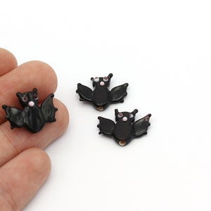 May include: Three black glass bat charms with white eyes and pink accents. The bats are approximately 1 inch in size.