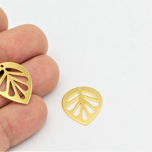 Pode incluir: Dois pingentes de folha de metal dourado com um design recortado. As folhas têm forma de lágrima com um furo na parte superior para prender em joias.