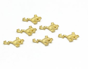 May include: Six gold-colored frog charms, each with a slightly different pose, are arranged on a white surface.