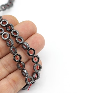 May include: A strand of black hematite beads with a hole in the center of each bead. The beads are strung on a red thread.