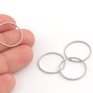 May include: Four silver jump rings, two are stacked on top of each other. The rings are textured and have a shiny finish.