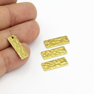 Könnte beinhalten: Vier rechteckige Anhänger aus goldfarbenem Metall mit strukturierter Oberfläche. Die Anhänger haben oben ein Loch zum Aufhängen.