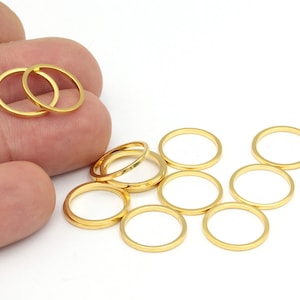 Op de afbeelding: Een set van tien gouden metalen springringen. De ringen zijn van verschillende groottes en liggen los op een wit oppervlak.