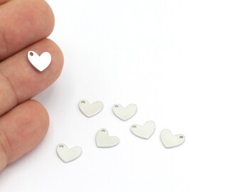 May include: A set of seven silver heart-shaped charms with a small hole at the top. The charms are arranged on a white surface.