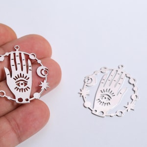 Può includere: Ciondoli argentati con un design a mano e occhio, circondati da stelle, lune e perline. Questi ciondoli sono progettati per la creazione di gioielli e progetti di artigianato.