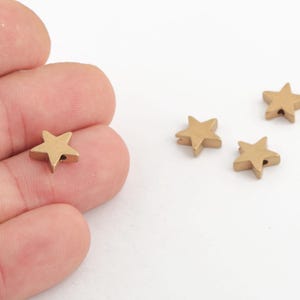 Puede incluir: Cuatro cuentas doradas en forma de estrella con un agujero en el centro. Las cuentas son pequeñas y tienen un acabado liso y brillante.