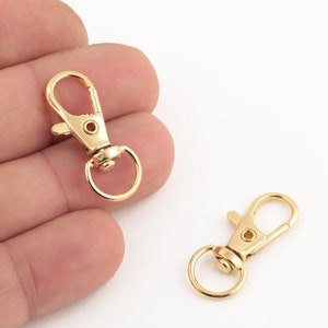 Puede incluir: Dos cierres giratorios de metal dorado con una puerta de resorte. Los cierres se utilizan comúnmente para sujetar llaveros, cordones o otros accesorios.