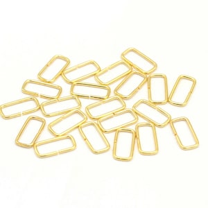 May include: A pile of gold-colored metal rings, each with a rectangular shape. The rings are scattered on a white surface.
