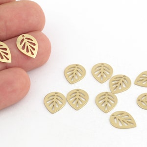 May include: Ten gold leaf charms with a cutout design. The charms are in the shape of a teardrop with a hole at the top for attaching to jewelry.