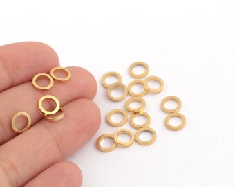 May include: A group of gold jump rings, some are in a hand, others are scattered on a white surface.