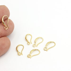 May include: Six gold-toned earring hooks, also known as ear wires, are displayed on a white surface. The hooks are made of metal and have a smooth, polished finish.