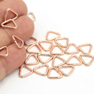 May include: A pile of rose gold triangle shaped metal rings. The rings are small and have a smooth finish.