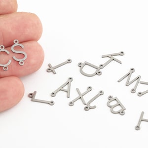 Peut inclure: Un ensemble de breloques en métal argenté en forme de lettres, comprenant les lettres A, B, C, D, H, I, J, K, L, M, S et X. Les breloques sont conçues pour être utilisées pour la fabrication de bijoux.